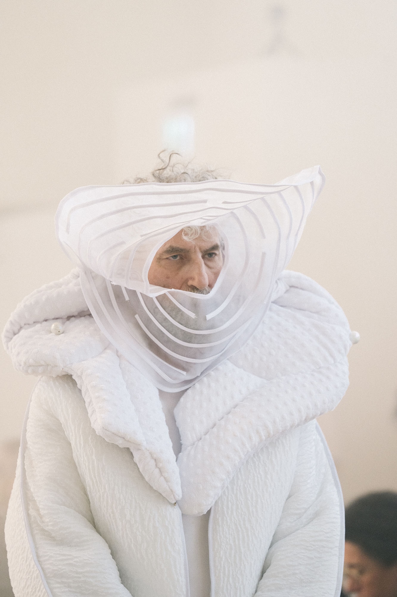 A close-up of a performer wearing a sculptural white garment framing the face in ANTICON.