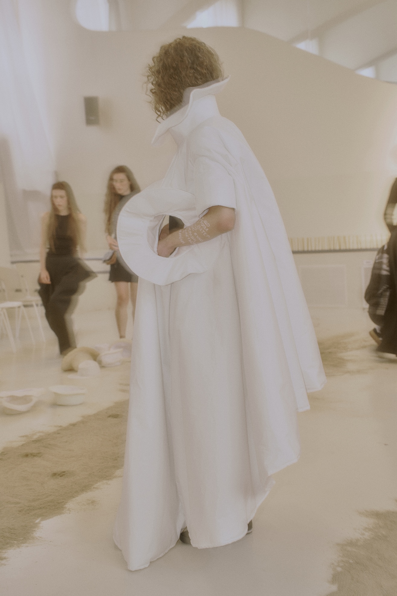 A side view of a performer in a white cape with a circular opening during ANTICON.