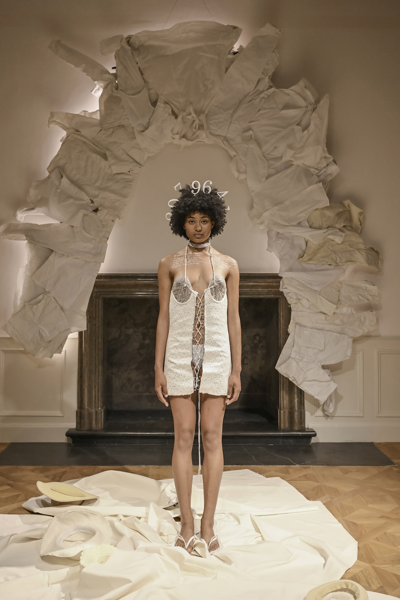 A performer presents a white garment with circular cut-outs against a sculptural backdrop.