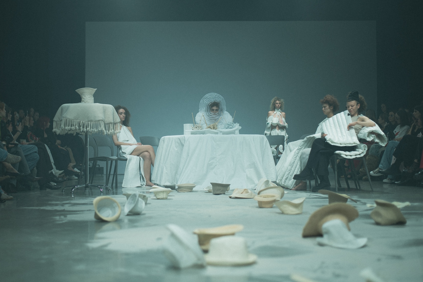 White-clad performers sit at a table on a blue-lit ANTICON stage.
